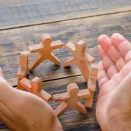 Business success concept on wooden background high angle view. hands protecting wooden figures of people.